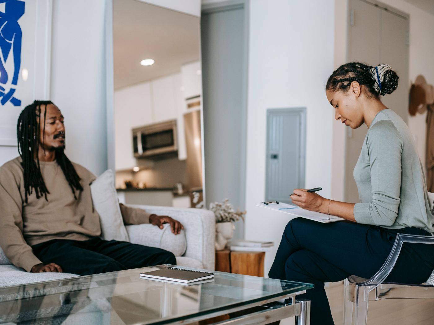 A therapist takes notes while a client speaks openly during an individual therapy session in a calm, home-like room.